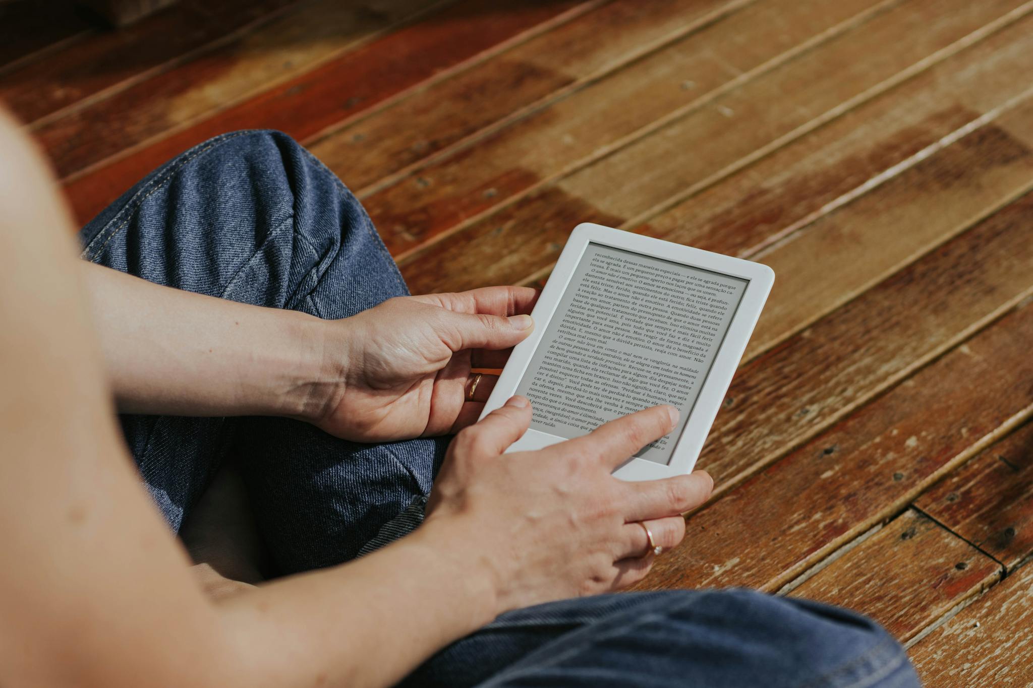 Close-up of hands holding an e-reader indoors on a wooden floor, emphasizing digital reading.