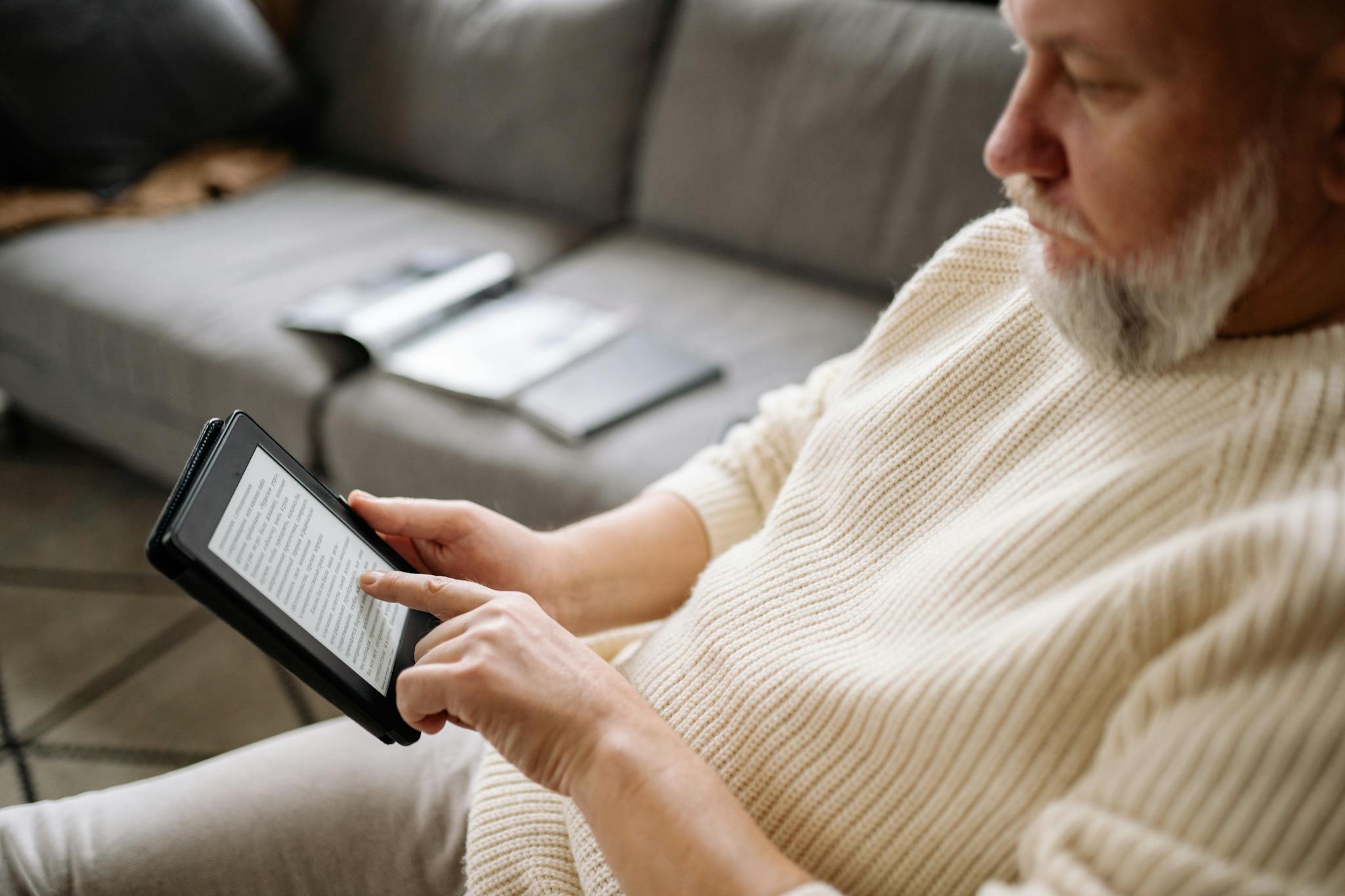 Elderly man using a tablet for reading in a cozy living room setting.